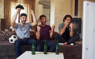 festeggiare vittoria. eccitato tre amici Guardando calcio su tv a casa insieme foto