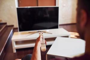 sostegno Visualizza di uomo detiene a distanza controllore nel mano e svolta su tv foto