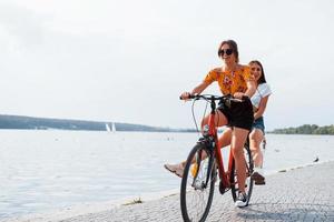 Due femmina amici su il bicicletta avere divertimento a spiaggia vicino il lago foto