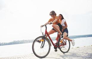 Due femmina amici su il bicicletta avere divertimento a spiaggia vicino il lago foto