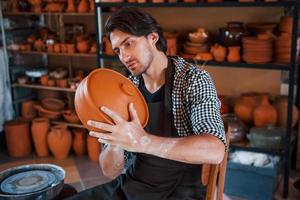 giovane ceramista detiene fresco fatto a mano Prodotto fatto di argilla nel mani e sembra a risultati di il suo opera foto