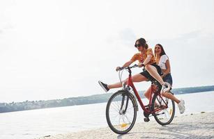 Due femmina amici su il bicicletta avere divertimento a spiaggia vicino il lago foto