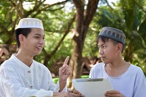 asiatico musulmano ragazzi sedersi insieme nel scuola parco per leggere e imparare loro quotidiano attività e fare compiti a casa nel loro gratuito volte prima andando indietro casa, morbido e selettivo messa a fuoco. foto