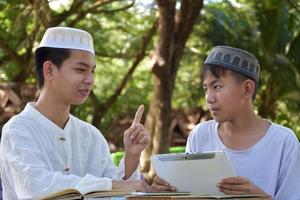 asiatico musulmano ragazzi sedersi insieme nel scuola parco per leggere e imparare loro quotidiano attività e fare compiti a casa nel loro gratuito volte prima andando indietro casa, morbido e selettivo messa a fuoco. foto