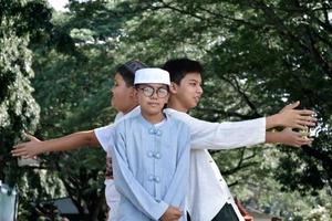 giovane asiatico musulmano ragazzi sollevato mani, smilling e abbracciare ogni altro per presente felicità sotto il alberi nel il parco, morbido e selettivo messa a fuoco. foto