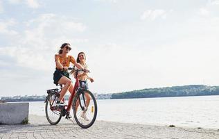 ragazza corre vicino bicicletta. Due femmina amici su il bicicletta avere divertimento a spiaggia vicino il lago foto