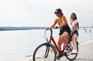 Due femmina amici su il bicicletta avere divertimento a spiaggia vicino il lago foto