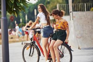 Due femmina amici su il bicicletta avere divertimento nel il parco vicino rampa foto
