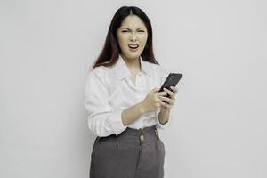 un' insoddisfatto giovane asiatico donna sembra scontento indossare bianca camicia irritata viso espressioni Tenere sua Telefono foto