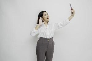 un' ritratto di un' contento asiatico donna indossare un' bianca camicia e Tenere sua Telefono, isolato di bianca sfondo foto