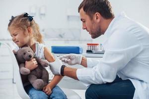 sangue campionamento. poco ragazza è nel il clinica con medico foto