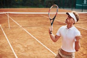 festeggiare vittoria. giovane tennis giocatore nel allegro Abiti è su il Tribunale all'aperto foto