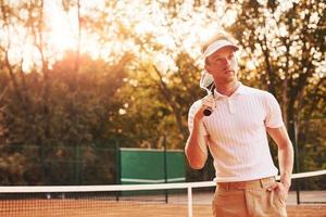 bellissimo luce del sole. giovane tennis giocatore nel allegro Abiti è su il Tribunale all'aperto foto