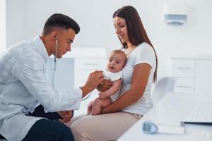 con La madre di aiuto. giovane pediatra è con poco bambino nel il clinica a giorno foto