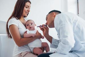 con La madre di aiuto. giovane pediatra è con poco bambino nel il clinica a giorno foto