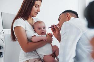 con La madre di aiuto. giovane pediatra è con poco bambino nel il clinica a giorno foto