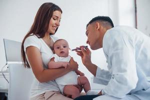 con La madre di aiuto. giovane pediatra è con poco bambino nel il clinica a giorno foto