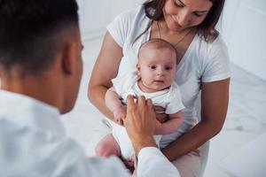 con La madre di aiuto. giovane pediatra è con poco bambino nel il clinica a giorno foto