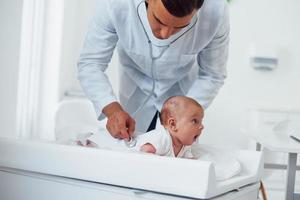 giovane pediatra è con poco bambino nel il clinica a giorno foto