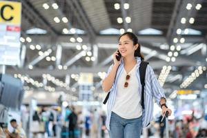 ritratto di un' giovane asiatico femmina viaggiatore utilizzando sua smartphone per contatto un' amico nel il partenza terminale. foto