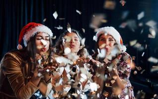 tre positivo ragazze soffiaggio oro colorato coriandoli a partire dal loro mani foto