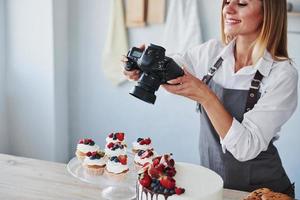 donna sta nel il cucina e prende foto di sua fatti in casa biscotti e torta di utilizzando telecamera