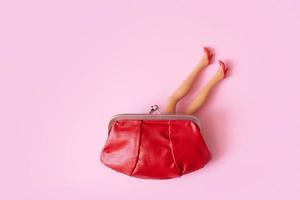 Bambola gambe nel rosso scarpe attaccare su di il borsa superiore Visualizza. creativo femmina shopping o finanza concetto foto
