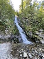 cascata fluente giù a partire dal il montagna per il roccioso riva di lago teletsky, altai, Russia foto