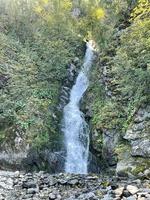 cascata fluente giù a partire dal il montagna per il roccioso riva di lago teletsky, altai, Russia foto