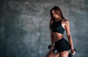 giovane fitness donna è nel il Palestra vicino parete con manubri nel mani foto