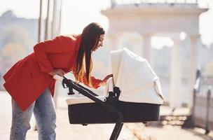 madre nel rosso cappotto avere un' camminare con sua ragazzo nel il carrozzina nel il parco a autunno tempo foto