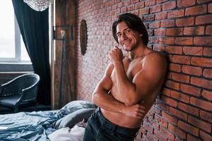 A petto nudo sexy uomo pendente su il mattone parete nel Camera da letto a mattina tempo foto
