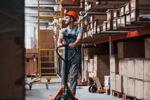 giovane maschio lavoratore nel uniforme è nel il magazzino con pallet camion foto