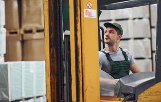 giovane lavoratore nel unifrom si siede nel il carrello elevatore a forca nel il magazzino foto