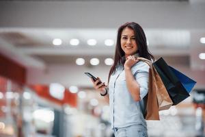brunetta donna nel il supermercato con molti di pacchi e Telefono nel mani avere shopping giorno