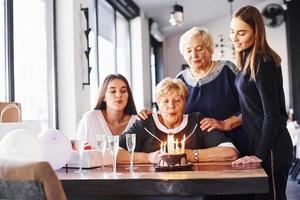 soffiaggio il candele. anziano donna con famiglia e amici festeggiare un' compleanno in casa foto