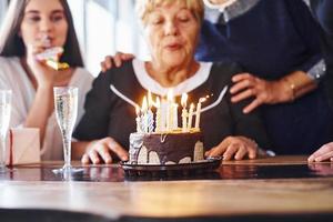 soffiaggio il candele. anziano donna con famiglia e amici festeggiare un' compleanno in casa foto