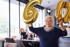 con palloncini di numero 60 nel mani. anziano donna con famiglia e amici festeggiare un' compleanno in casa foto