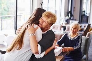 Abbracciare una persona ogni Altro. anziano donna con famiglia e amici festeggiare un' compleanno in casa foto