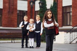 gruppo di bambini nel scuola uniforme in posa per il telecamera all'aperto insieme vicino formazione scolastica edificio foto