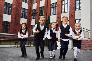 gruppo di bambini nel scuola uniforme in posa per il telecamera all'aperto insieme vicino formazione scolastica edificio foto