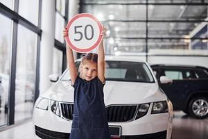 ritratto di carino poco ragazza quello detiene strada cartello nel mani nel automobile salone foto