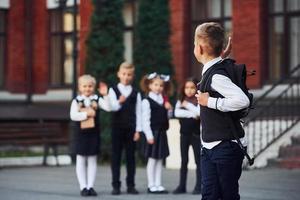 gruppo di bambini nel scuola uniforme in posa per il telecamera all'aperto insieme vicino formazione scolastica edificio foto