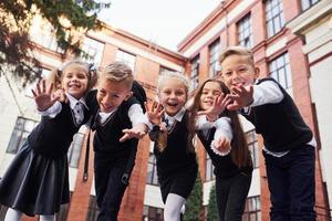 avendo divertimento e Abbracciare una persona ogni Altro. gruppo di bambini nel scuola uniforme quello è all'aperto insieme vicino formazione scolastica edificio foto