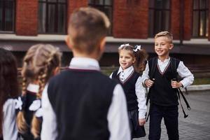 avere un' incontro. gruppo di bambini nel scuola uniforme quello è all'aperto insieme vicino formazione scolastica edificio foto