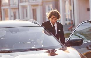 ritratto di bello giovane uomo d'affari nel nero completo da uomo e cravatta all'aperto vicino moderno auto nel il città foto