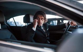 giovane uomo d'affari nel nero completo da uomo e cravatta guida moderno automobile foto