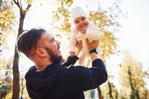 simpatico luce del sole. padre nel casuale Abiti con il suo bambino è nel il bellissimo autunno parco foto