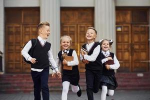 gruppo di bambini nel scuola uniforme quello è in esecuzione all'aperto insieme foto