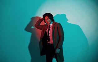 ritratto di giovane elegante uomo nel cappello, completo da uomo e cravatta quello sta nel neon luci nel il studio foto